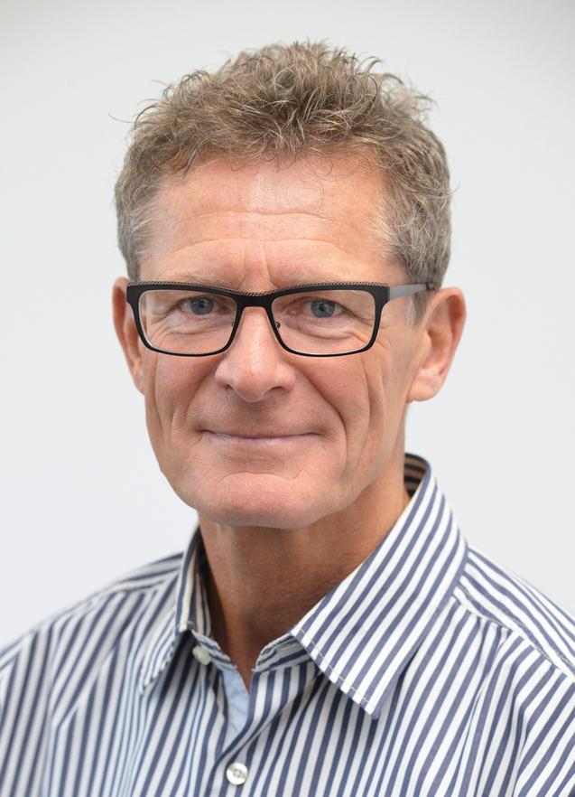 Uwe Göbel Porträt eines Mannes mit kurzen, lockigen Haaren und Brille, der ein gestreiftes Hemd trägt, vor neutralem Hintergrund.