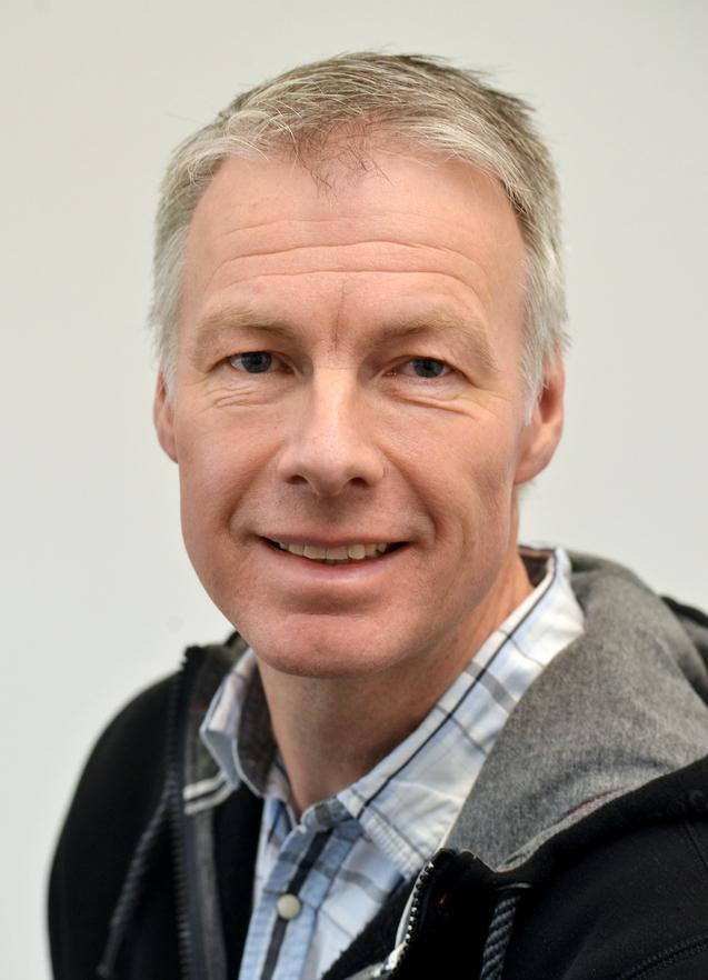 Stefan Wernsmann Portrait eines Mannes mit kurzem grauen Haar, in einem schwarz-grauen Pulli und kariertem Hemd, vor einem hellen Hintergrund.